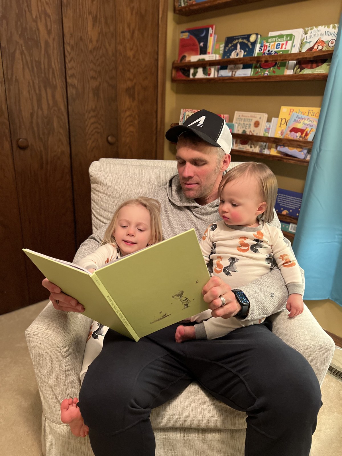 A parent in an armchair reads What Do You Do With an Idea? to two young children, with picture books on wall ledges behind them.